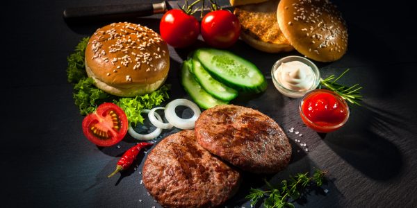 Grilled beef patties with other ingredients for hamburgers Homemade hamburger. Grilled beef patties, sesame buns with other ingredients for hamburgers on dark slate plate